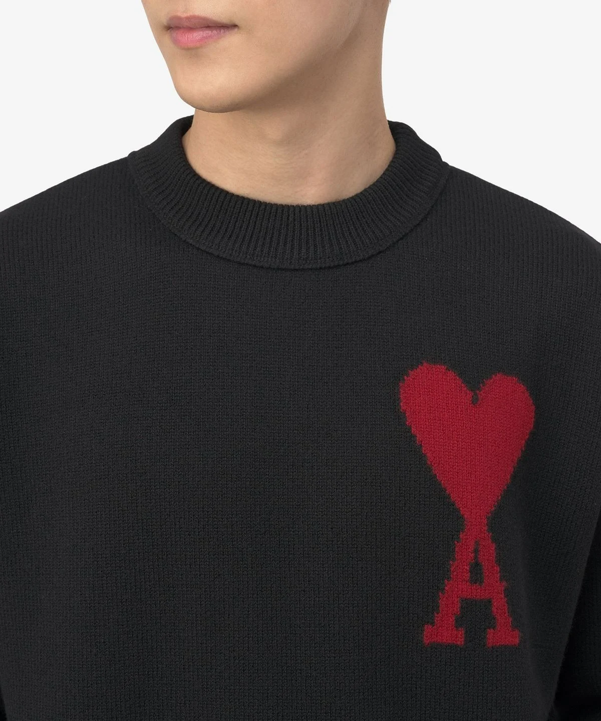 니트의 촘촘한 짜임과 레드 하트 로고의 정교한 인타르시아 마감을 근접 촬영한 모습